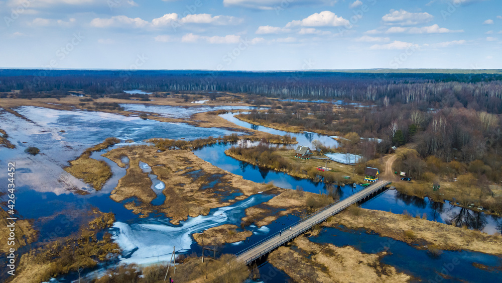 Aerial landscape view on river with flooded meadows and beautiful fields.. Wooden bridge over small river in spring. Travel concept.