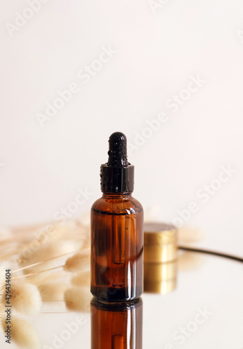 Glass cosmetic brown bottle with a dropper on a beige background with dry flowers . The concept of natural cosmetics, natural essential oil