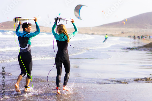 Happy couple going to surf on tropical beach.  Friends having fun doing extreme sport. Joyful people and healthy lifestyle concept.