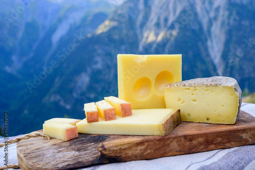 Cheese collection, French beaufort, abondance, emmental, tomme de savoie cheeses served outdoor in Savoy region, with Alpine mountains peaks on background photo