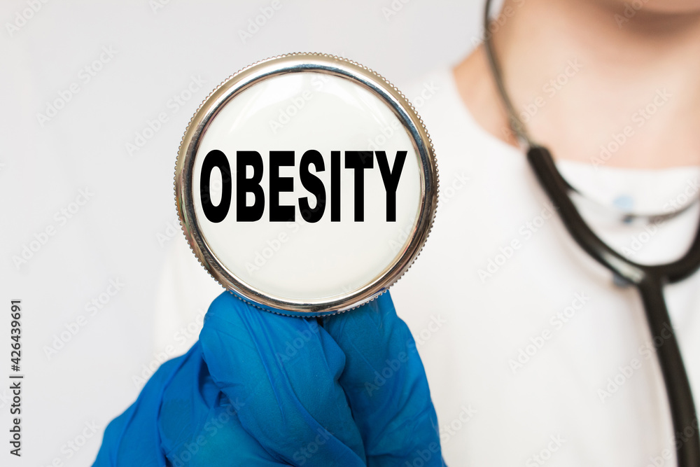 The doctor's blue - gloved hands show the word OBESITY - . a gloved hand on a white background. Medical concept. the medicine The doctor's blue - gloved hands show the word OBESITY - . a gloved hand on a white background. Medical concept. the medicine