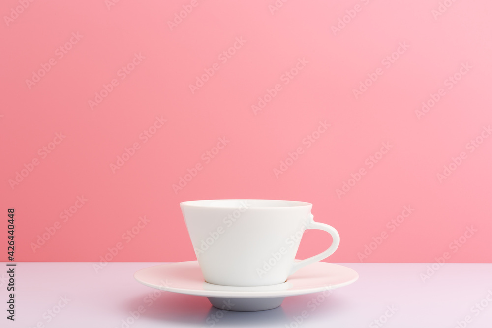 Fototapeta premium White ceramic coffee cup with saucer on white table against light pink background with copy space