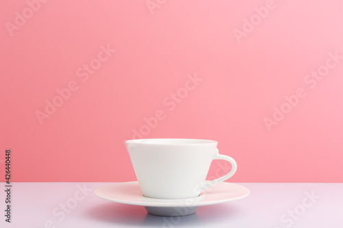 White ceramic coffee cup with saucer on white table against light pink background with copy space