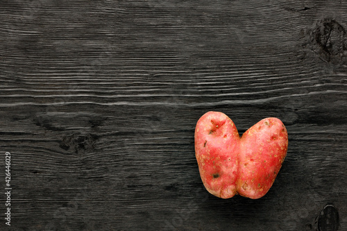 Heart shaped ugly potatoes on a black wooden gnarled background. Vegetable or food waste concept.