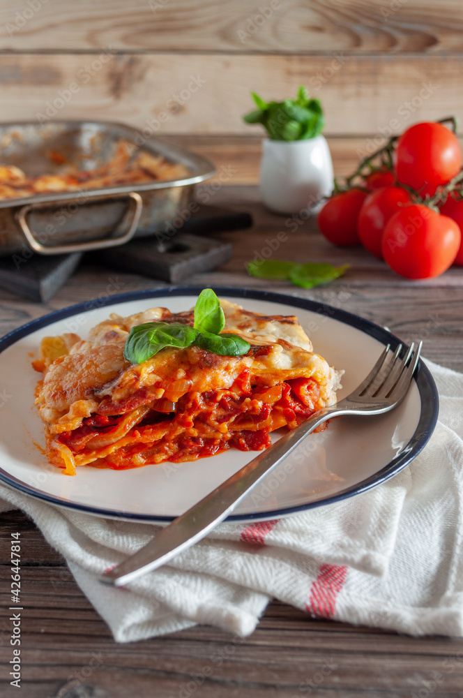 Lasagna with balanese sauce and basil served on a platter next to a baking dish on a light wooden background Lasagna with balanese sauce and basil served on a platter next to a baking dish on a light wooden background