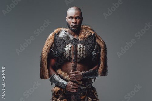 Bearded black skinned barbarian with fur and shaved head holding an axe