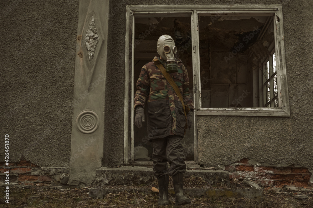 A man in a gas mask comes out of a destroyed house - a post-apocalyptic image of the future in a world with a polluted ecology A man in a gas mask comes out of a destroyed house - a post-apocalyptic image of the future in a world with a polluted ecology