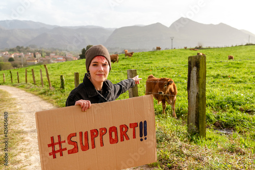 vegan animal rights activist poses with a support sign in front of livestock. young girl asking for support.