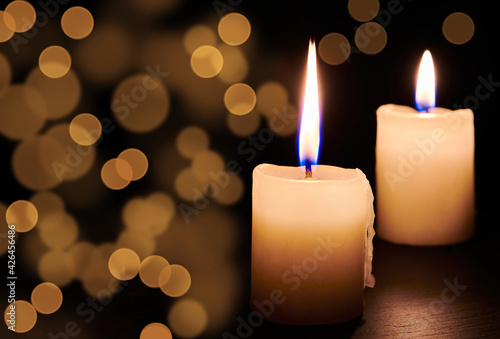 Two burning candles on the table in night dark. Candle lights in darkness and bokeh light effects for solemn moments and holidays. Close up view with copy space.