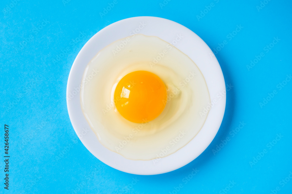 Raw egg on a white plate. View from above. Fresh egg with a bright yolk on a blue background. Raw egg on a white plate. View from above. Fresh egg with a bright yolk on a blue background.