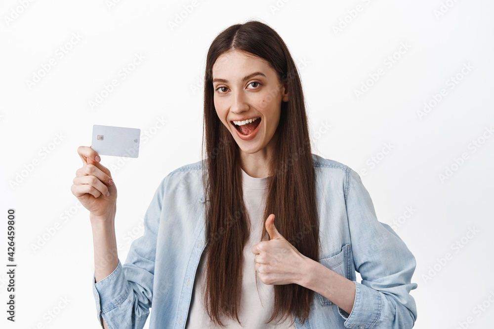 Image of female student say yes, showing credit card and thumb up, approve and recommend bank, easy contactless payment, standing over white background Image of female student say yes, showing credit card and thumb up, approve and recommend bank, easy contactless payment, standing over white background