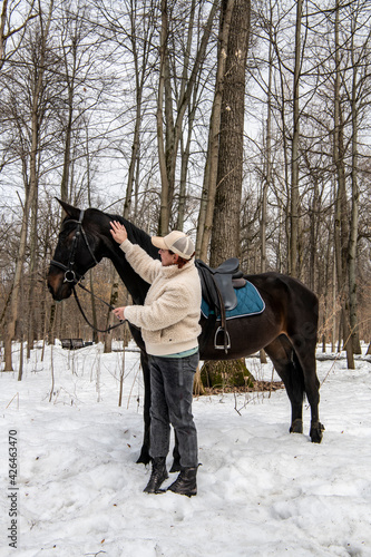 woman in beige jacket and cap with black horse in spring park 