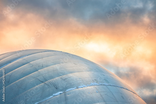 Blue dome under dramatic sunset sky. Spherical building. Beautiful Soft Orange Yellow Evening light. Cloudy day. Colorful sky. Cupola. Minimalism. Negative space. Colorful sky at sunrise. Morning. 