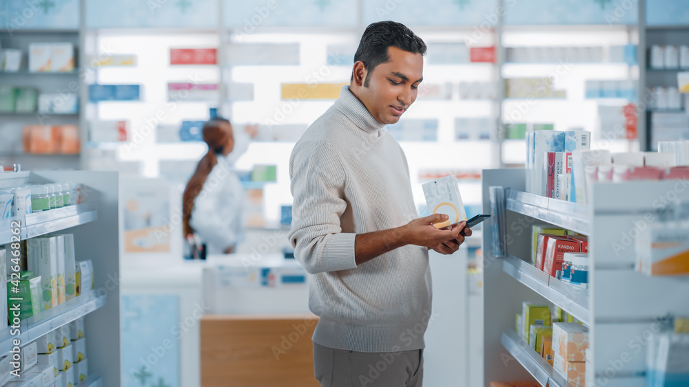 Pharmacy Drugstore: Portrait of a Handsome Young Indian Man Using Smartphone Device, Chooses to Purchase Best Medicine, Drugs, Vitamins. Shelves full of Sport Supplements, Health Care Products Pharmacy Drugstore: Portrait of a Handsome Young Indian Man Using Smartphone Device, Chooses to Purchase Best Medicine, Drugs, Vitamins. Shelves full of Sport Supplements, Health Care Products