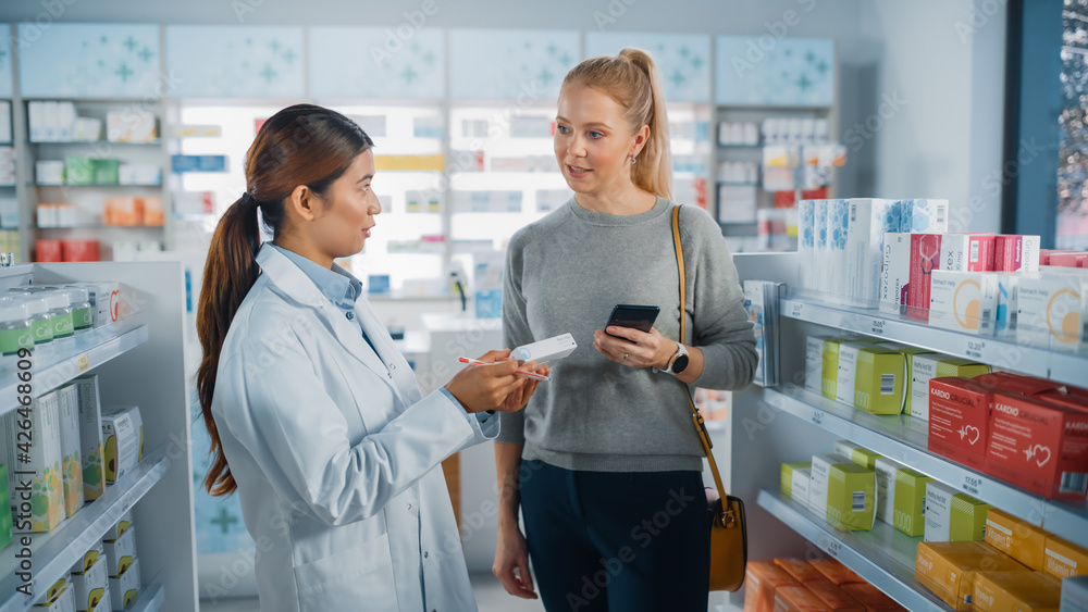 Pharmacy Drugstore: Caucasian Woman Chooses to Buy Medicine Professional Asian Pharmacist Advising, Consulting, Recommending Customer the Best Option. Modern Pharma Store Health Care Products