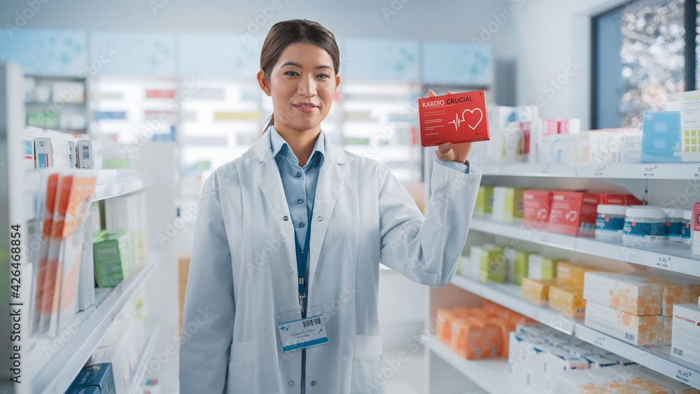 Pharmacy Drugstore: Portrait of Professional Asian Female Pharmacist Holding Showing Box of Pills, Looking at Camera, Smiling. Store with Health Care Products, Specialist Recommending Best Product.