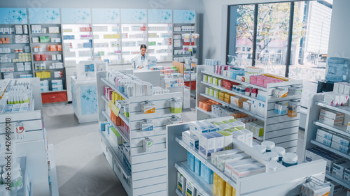 Big Modern Pharmacy Drugstore with Shelves full of Packages Full of Modern Medicine, Drugs, Vitamin Boxes, Pills, Supplements, Health Care Products. Pharmacist Standing at Counter.