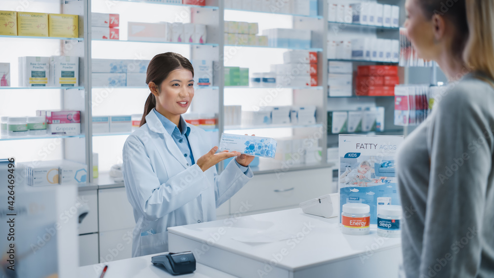 Pharmacy Drugstore Checkout Cashier Counter: Professional Asian Female Pharmacist Recommends Medicine in a Package for a Beautiful Caucasian Female Customer.
