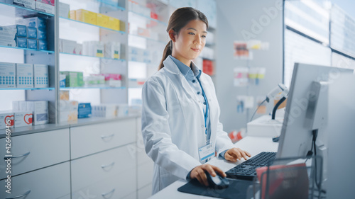 Pharmacy Drugstore: Beautiful Asian Pharmacist Uses Checkout Counter Computer, Does Inventory Checkup, Online Prescription of Medicine Packages, Drugs, Vitamin Boxes, Supplements, Health Care Products photo
