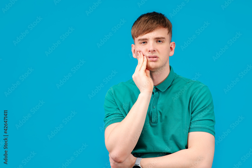 Young guy, a man suffering from toothache, holds his cheek with his hand. On a blue, monochrome background in the studio. Young guy, a man suffering from toothache, holds his cheek with his hand. On a blue, monochrome background in the studio.