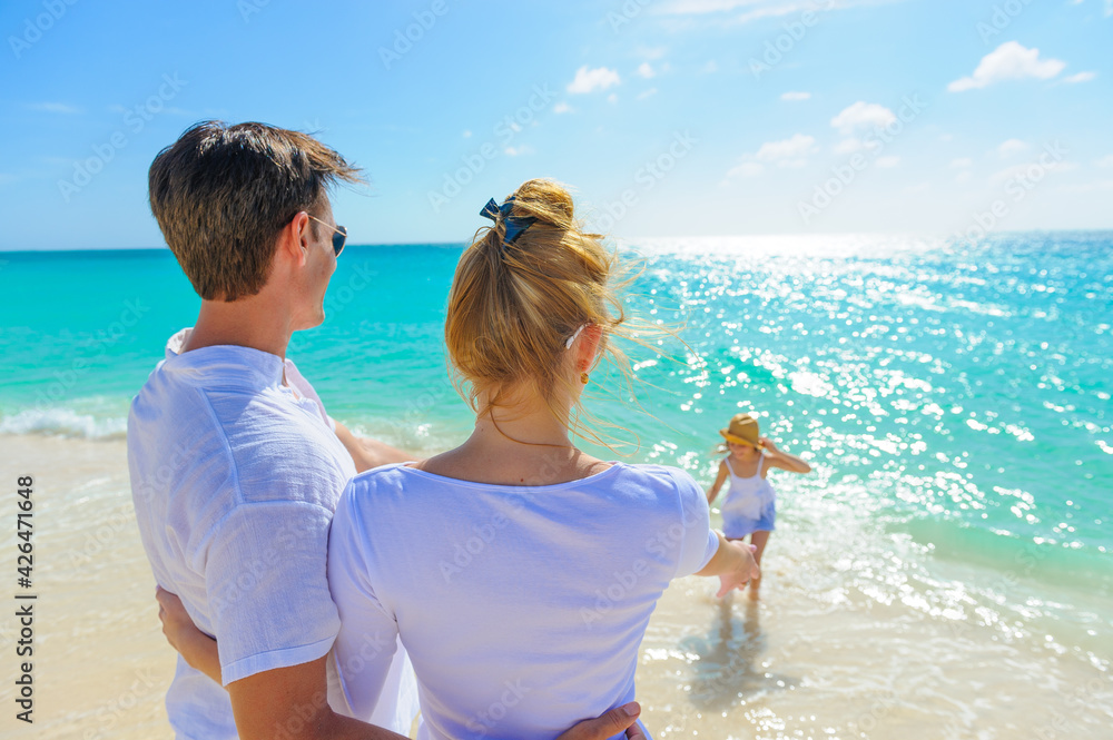 Family at the beach, mother, father and daughter playing on the sand dressed in white tropical outfits Family at the beach, mother, father and daughter playing on the sand dressed in white tropical outfits