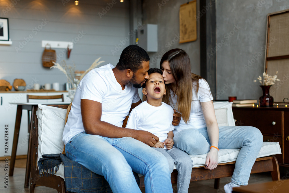 © Kanstantsinzzz - Loving black family relaxing at sofa in the morning, happy mixed race parents laughing cuddling having fun with cute little kid child son playing enjoying moments together. High quality photo