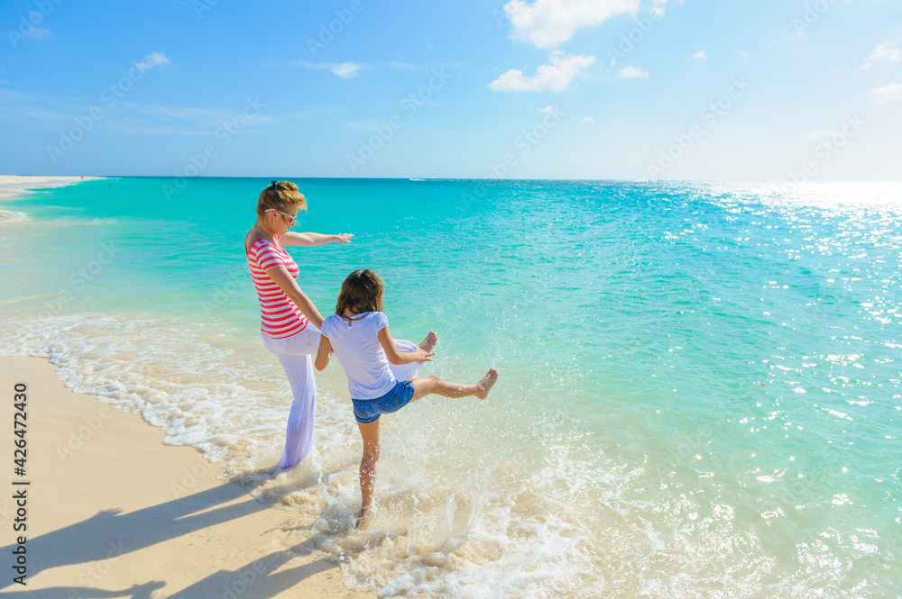 Family at the beach, mother and daughter standing on the shore while holding hands