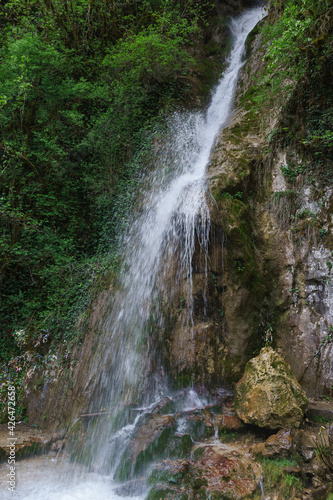 From the height of the stream flows clear water-a beautiful waterfall Maiden Tears in Bzyb gorge of Abkhazia. Colorful ribbons hang on the branches of trees - a ritual for good luck