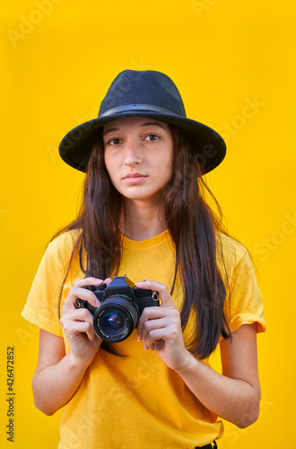 Vertical photo of a young girl with a photo camera on yellow background