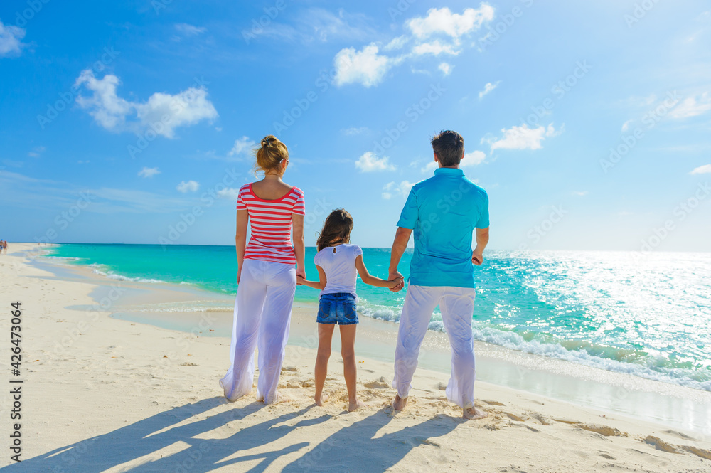 Family at the beach, mother, father and daughter holding hands on the seashore and dressed in colorful tropical outfits