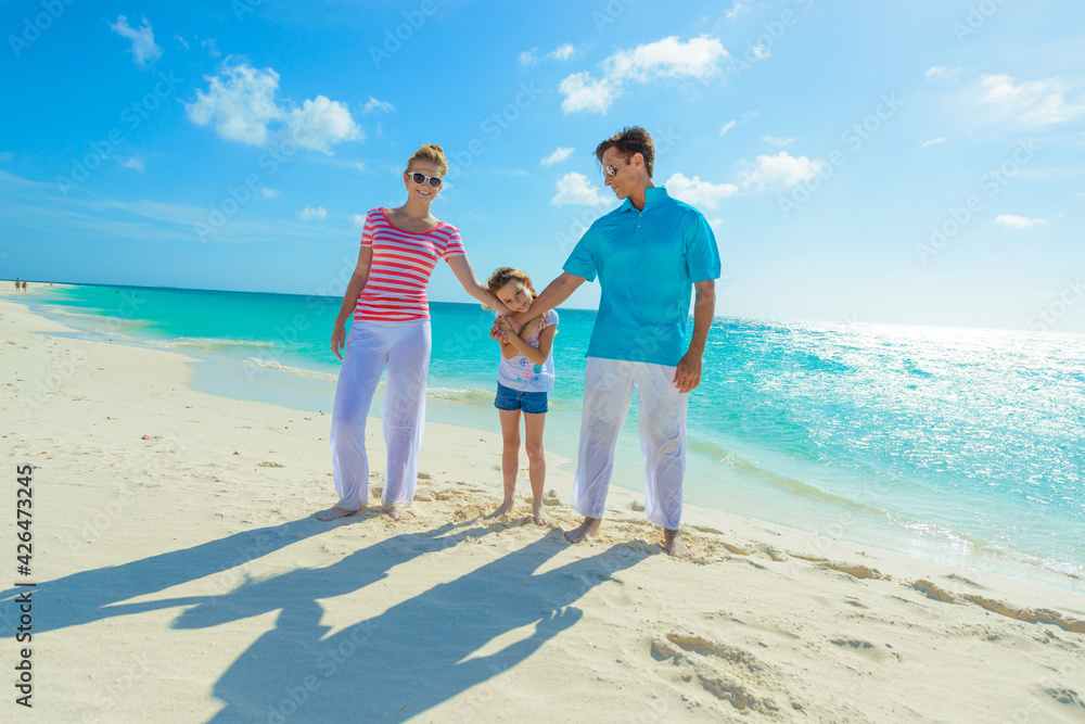 Family at the beach, mother, father and daughter playing on the sand dressed in colorful tropical outfits Family at the beach, mother, father and daughter playing on the sand dressed in colorful tropical outfits