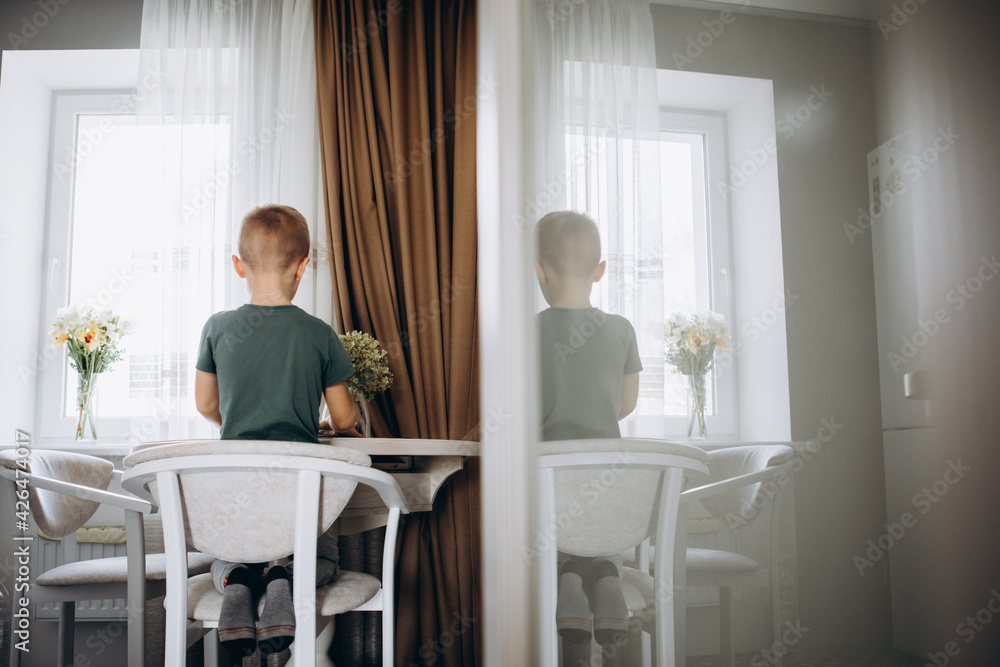 The boy plays computer games on the tablet in the kitchen. The boy plays computer games on the tablet in the kitchen.