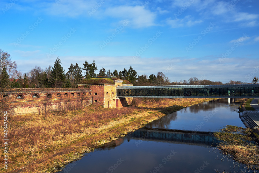 a modern footbridge and historic defensive walls on the Warta River