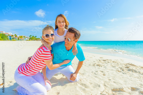 Family at the beach, mother, father and daughter playing on the sand dressed in colorful tropical outfits