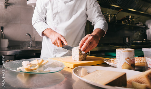 Chef's hands detail while slicing cheese on wooden cutting board