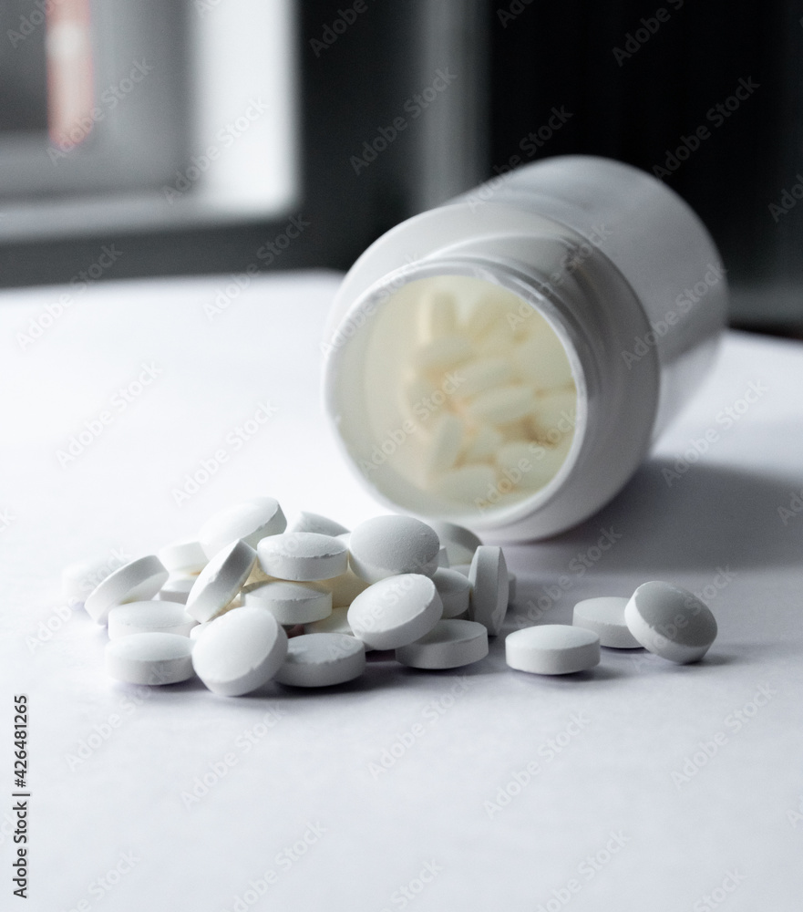 White bottle of white pills overturned on the table White bottle of white pills overturned on the table