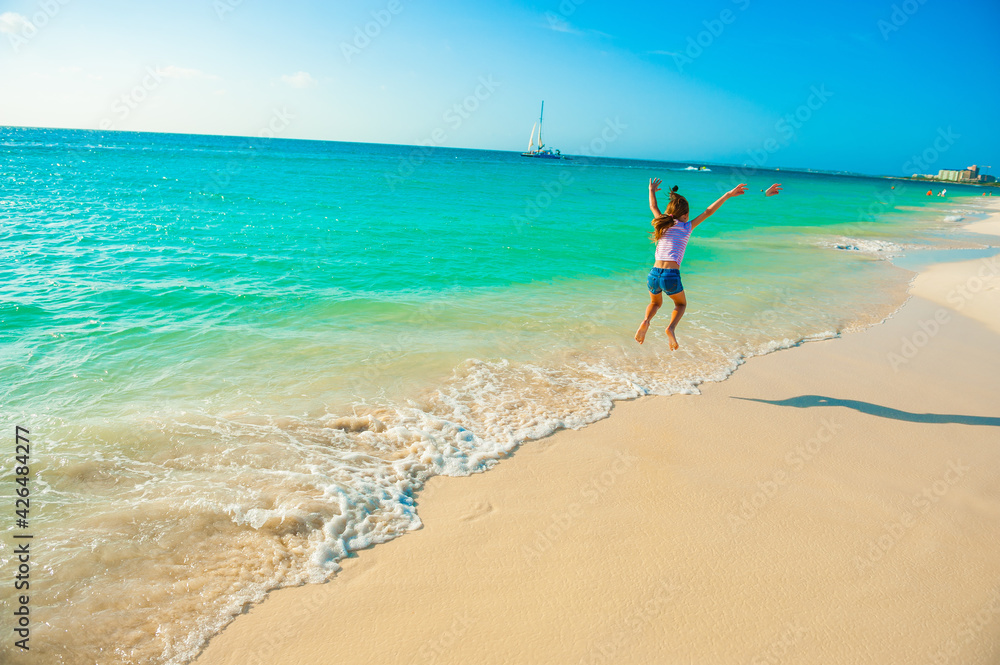 Young girl at the beach, playing, running on the shore, dressed in colorful tropical outfit Young girl at the beach, playing, running on the shore, dressed in colorful tropical outfit