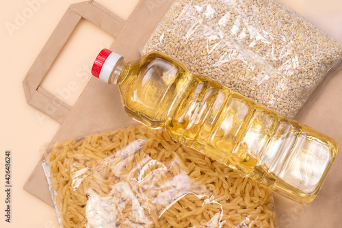 Paper bag with food supplies crisis food supply on a light yellow background. Pearl barley, pasta, sunflower oil. Food delivery, Donation, coronavirus