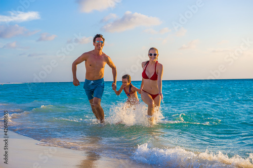 Family at the beach, mother, father and daughter running on the shoreline while holding hands