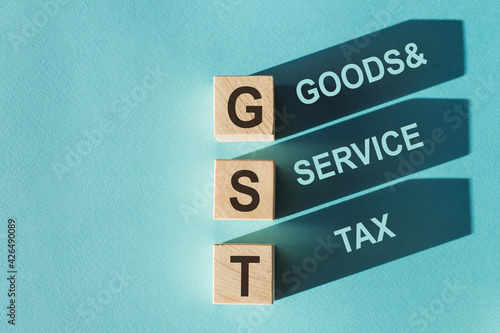 Wooden cubes building word GST - (abbreviation of goods and services tax) on light blue background.