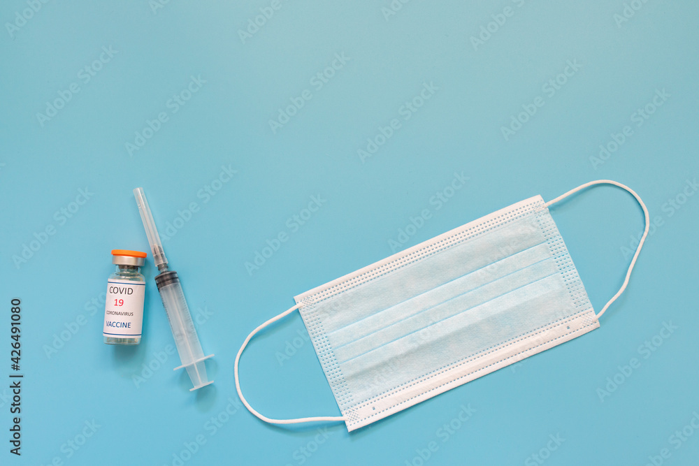 Protective medical mask, syringe and covid 19 vaccine on a blue background. The concept of vaccination, immunization,prevention of people from Covid. Protective medical mask, syringe and covid 19 vaccine on a blue background. The concept of vaccination, immunization,prevention of people from Covid.