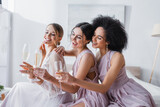 joyful bride and bridesmaids sitting in bedroom with champagne glasses.