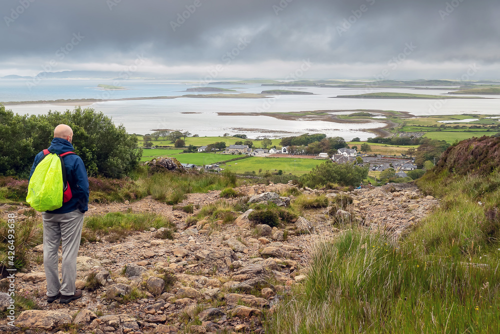Bald male tourist with backpack looking at beautiful scenery. Westport, county Mayo, Ireland. Foot path to Croagh Patrick. Irish nature and travel concept