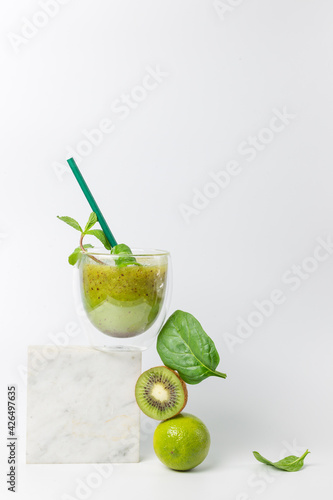 Refreshing detox smoothie with kiwi, lime, mint and spinach on a marble stand. The concept of a balanced diet. On a white background, vertically.