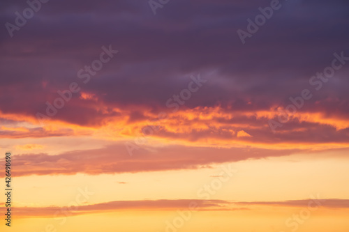 Bright violet or purple clouds at epic orange sunset sky background. © DedMityay