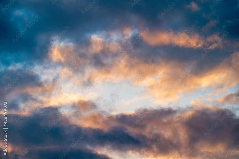 Colorful cloudy sky background, sunset cloudscape with blue overcast as frame and and light yellow-orange heaven in center, abstract nature background copy space.
