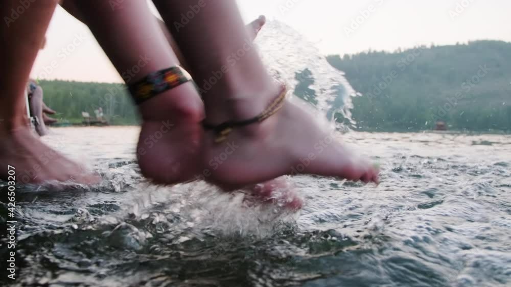 Close up shot of legs of unrecognizable man and woman sitting on pier and splashing lake water with feet Close up shot of legs of unrecognizable man and woman sitting on pier and splashing lake water with feet