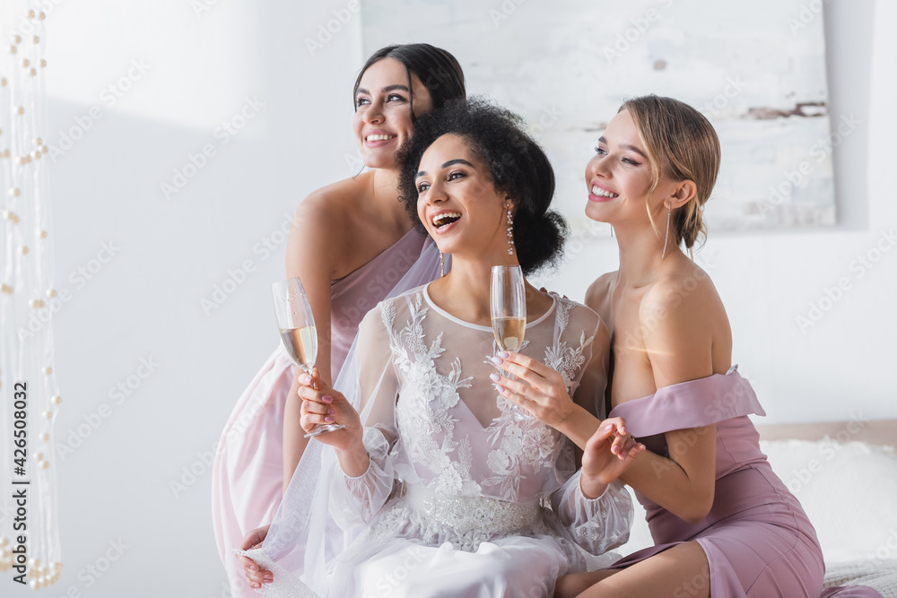 excited african american bride holding champagne near happy bridesmaids.
