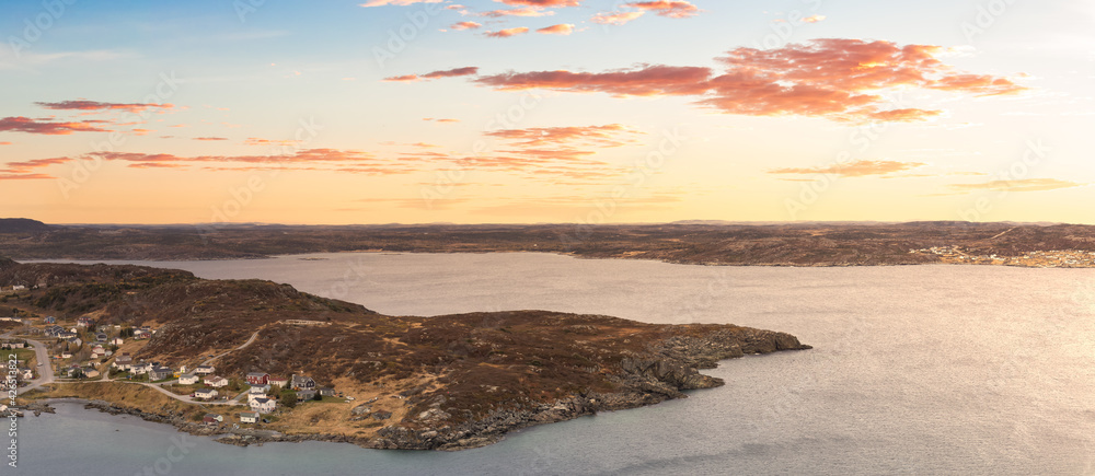 Fototapeta premium Aerial panoramic view of a town on the Rocky Atlantic Ocean Coast. Colorful Sunrise Sky Art Render. Taken in St. Anthony, Newfoundland, Canada.