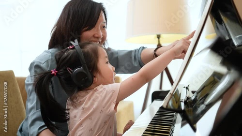 Medium close up shot of Asian mother and daughter practice piano together with happy and fun,  Music class learning at home.